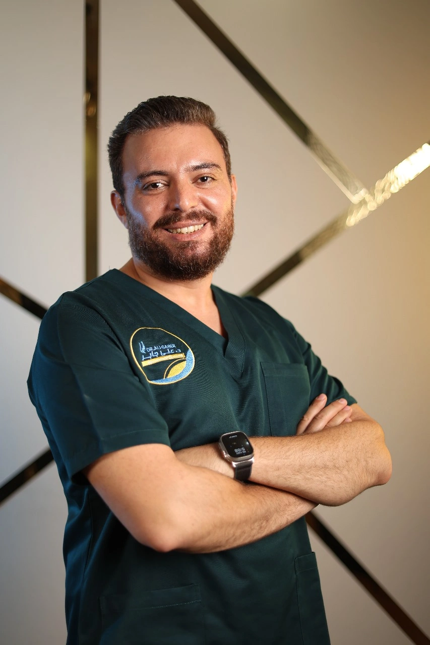 Portrait of a smiling doctor in green scrubs with arms crossed.