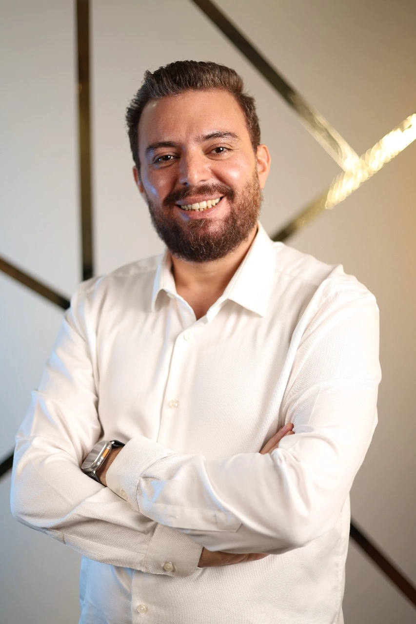 Smiling doctor in a white shirt and watch with arms folded.